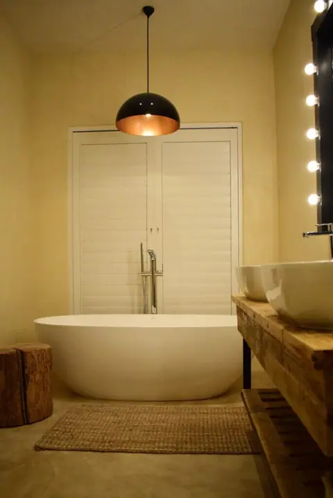 Free-standing bath and wooden vanity under a copper pendant